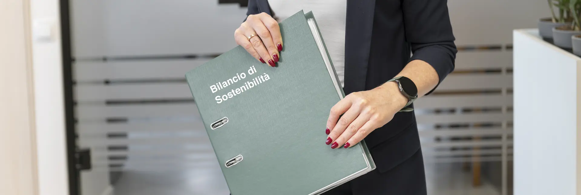 Una persona in abito formale tiene in mano un raccoglitore con la scritta "Bilancio di Sostenibilità"